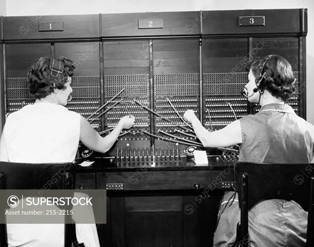 Rear view of two female telephone operators operating a telephone switchboard