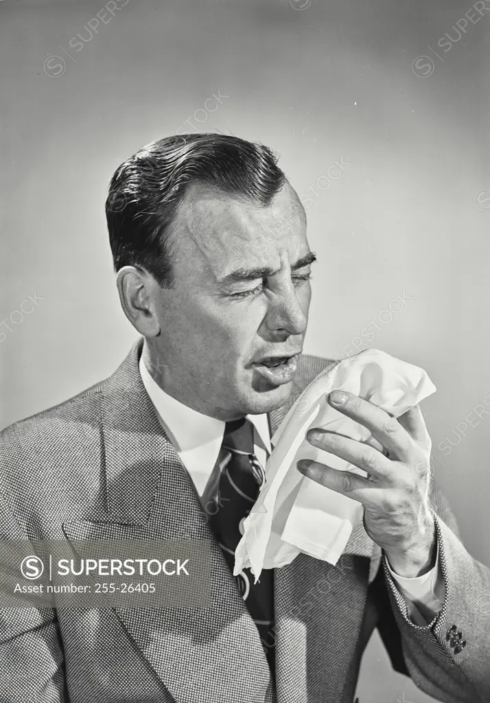 Vintage photograph. Man in suit and tie sneezing into handkerchief