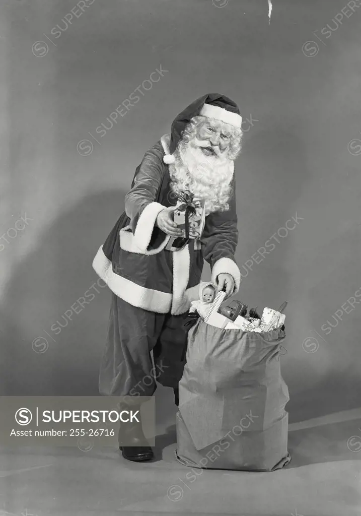 Vintage photograph. Man in Santa Claus costume grabbing Christmas toys from sack