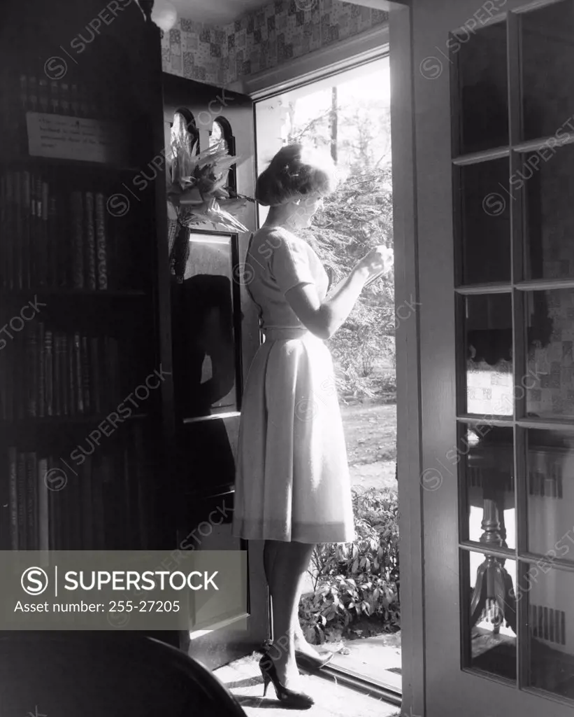 Side profile of a young woman standing at the door holding a letter