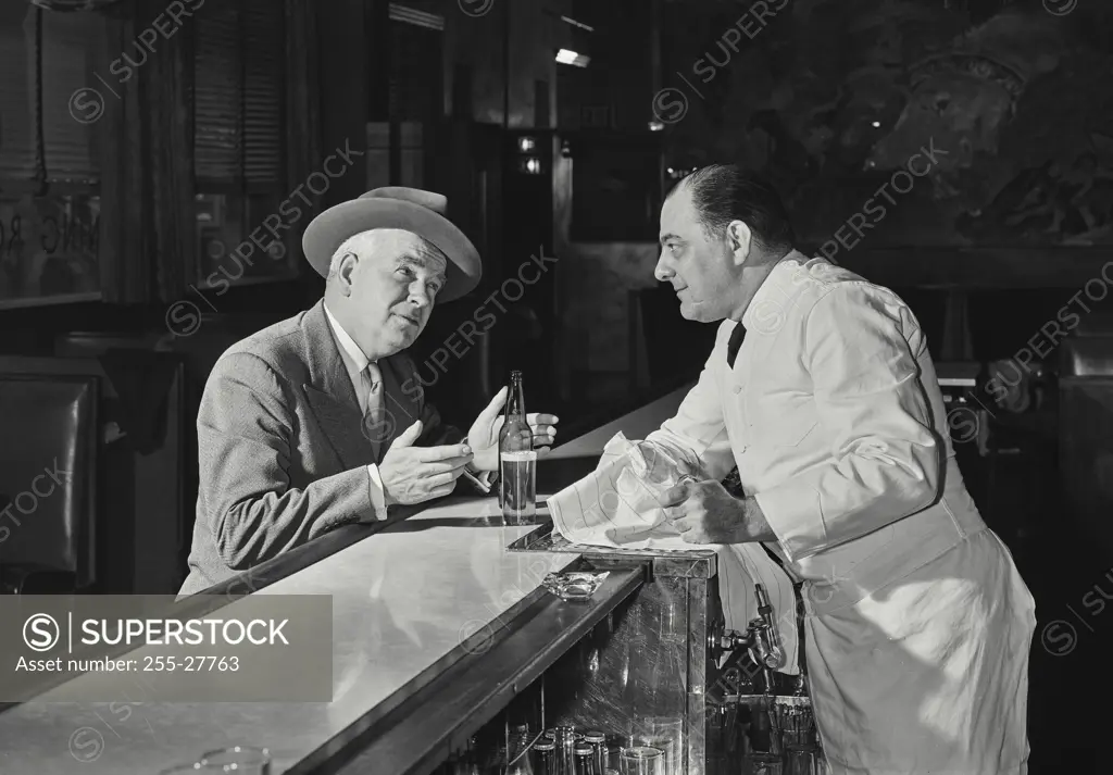 Vintage Photograph. Man in suit sitting at bar talking to bartender. Frame 1