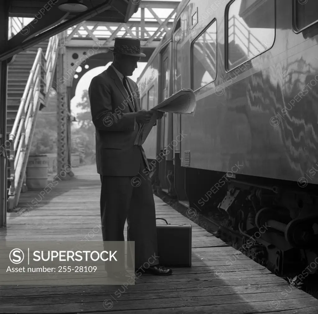 Businessman reading newspaper on railroad platform