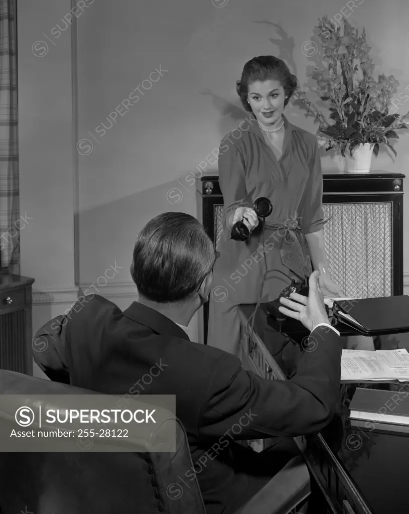 Secretary giving phone receiver to boss in office