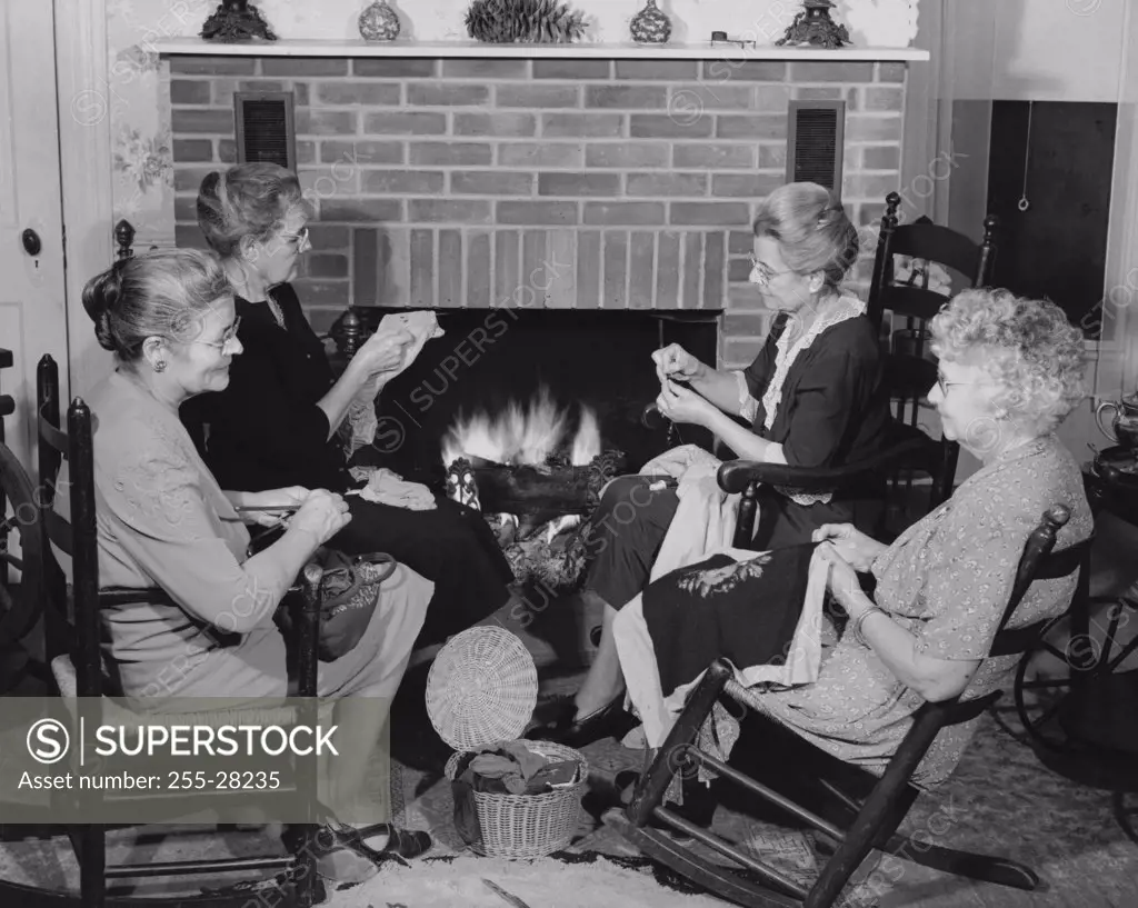 Senior women sitting in chairs near a fireplace and knitting