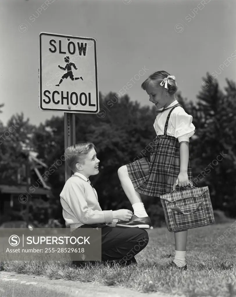 Vintage Photograph. Young boy tying young girls shoe at bus stop