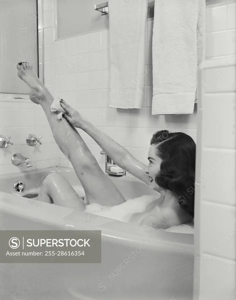 Vintage Photograph. Woman in bathtub leaning back and raising leg up to clean with washcloth