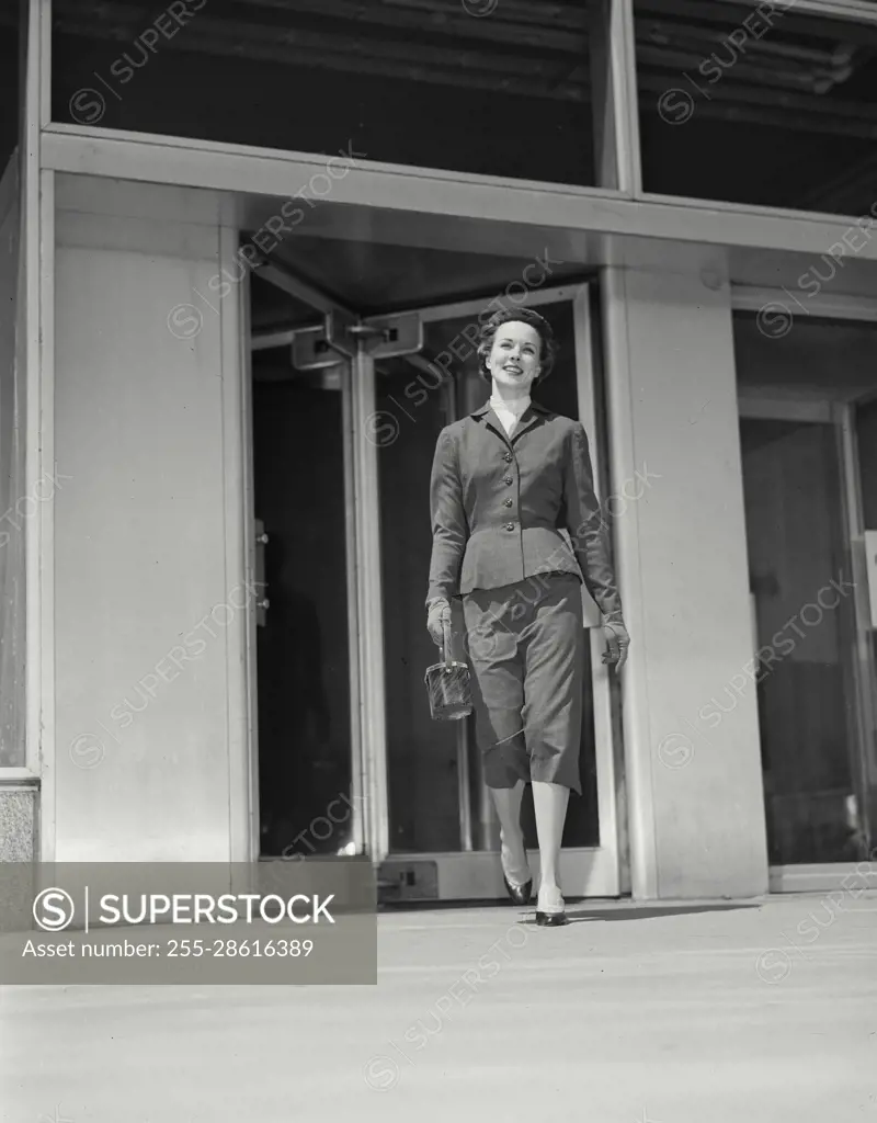 Vintage Photograph. Fashionable woman walking away from revolving doors of building