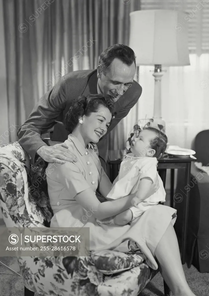 Vintage Photograph. Parents in living room holding and looking at baby. Frame 2