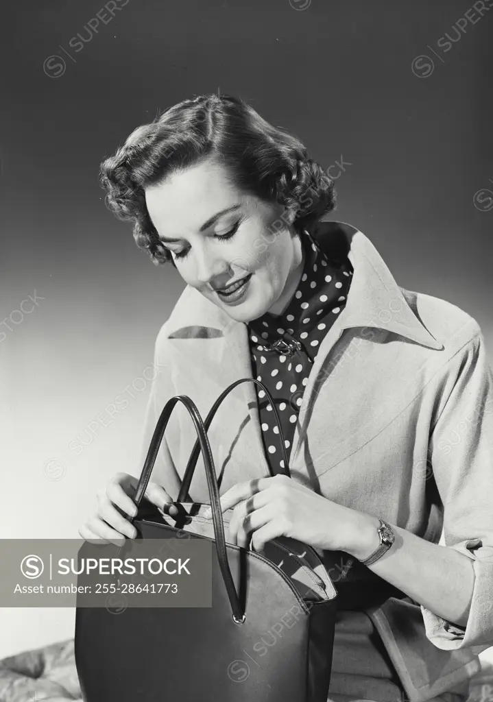 Vintage Photograph. Woman with curly hair wearing coat with wide collar over polka dot blouse looking in purse, Frame 1