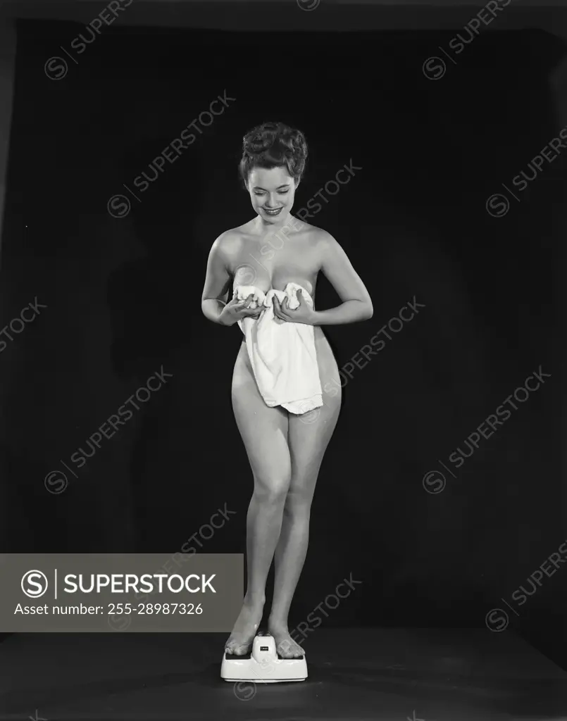 Vintage Photograph. Young nude woman with bath towel standing on scale in  front of black background - SuperStock