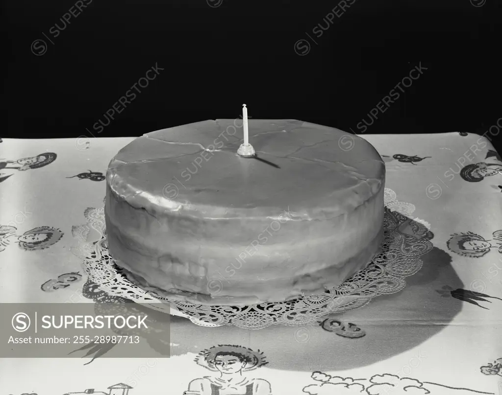 Vintage Photograph. Cake on lace doily with one candle on table with tablecloth