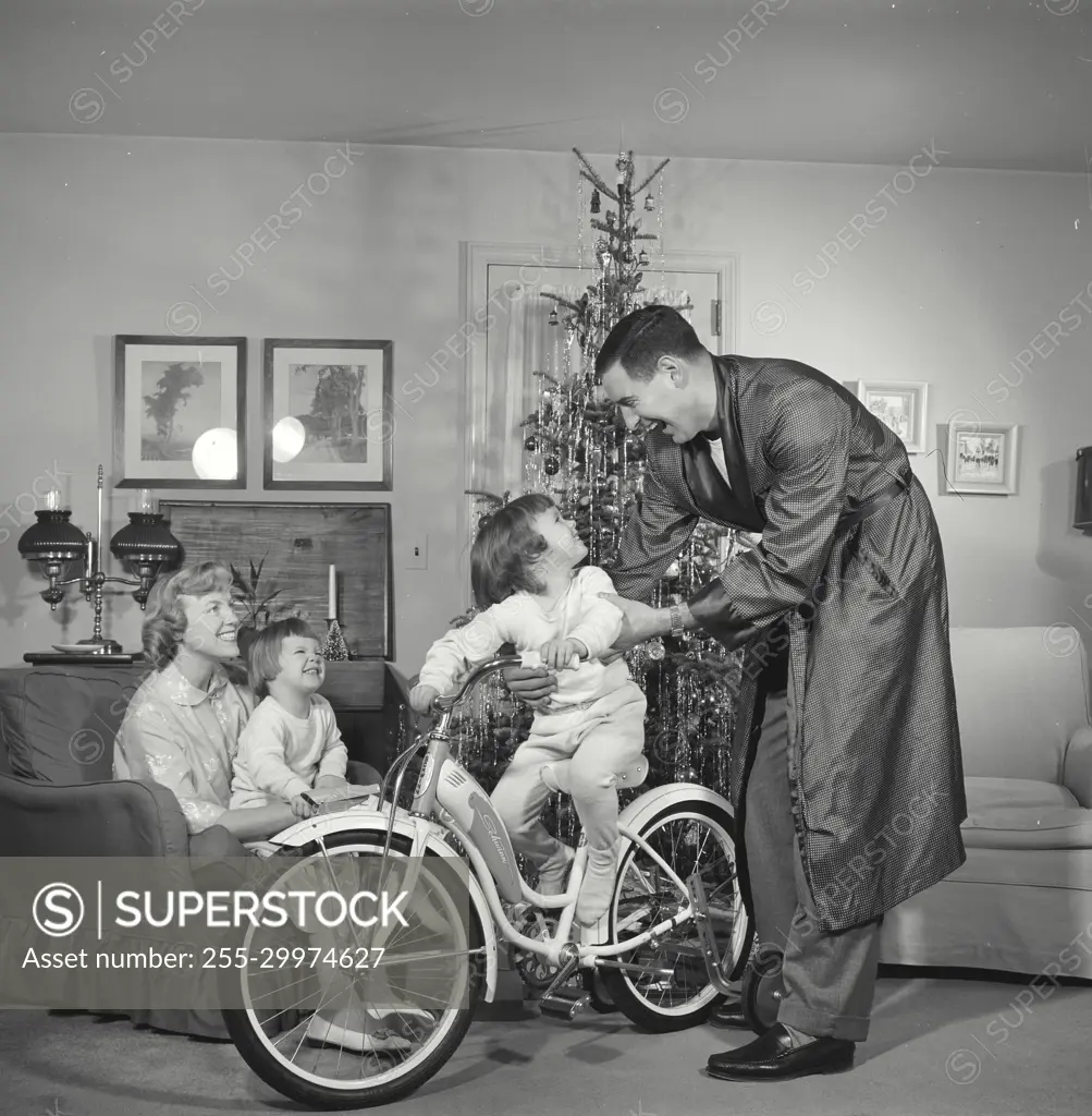 Vintage Photograph. Family gathered around Christmas tree father and child play with bicycle.