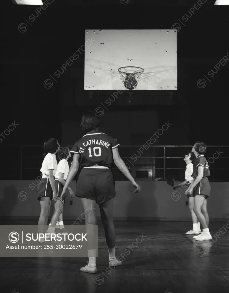 Vintage Photograph. Basket ball goes in hoop while players stand around free-throw perimeter.