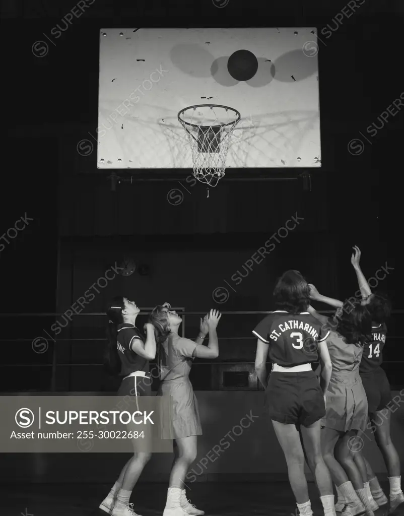 Vintage Photograph. Basketball is near hoop while female players are gathered underneath.