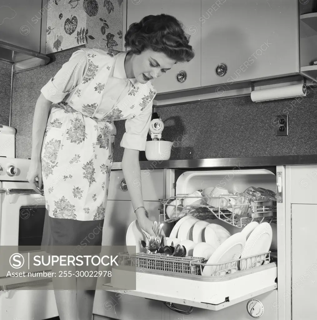 Vintage Photograph. Woman loads knives into dishwasher.