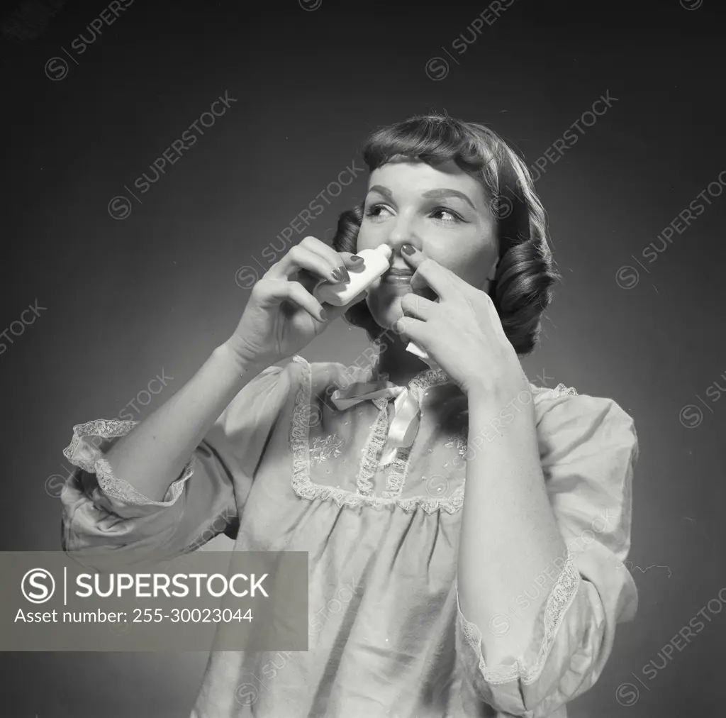 Vintage Photograph. Woman smiles while putting nose spray into her nose.