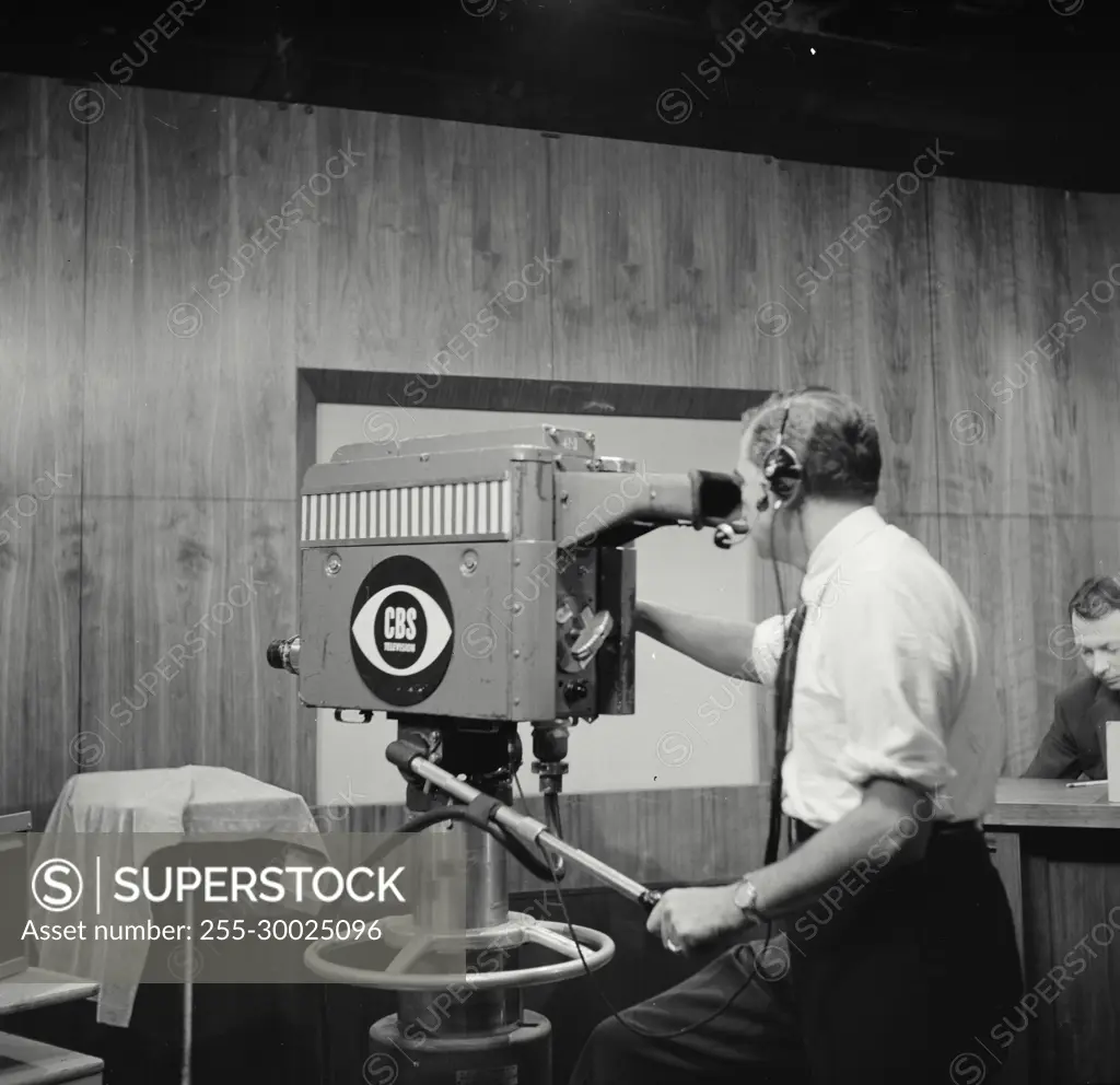 Vintage Photograph. Man operates CBS Television camera in studio from rear view.