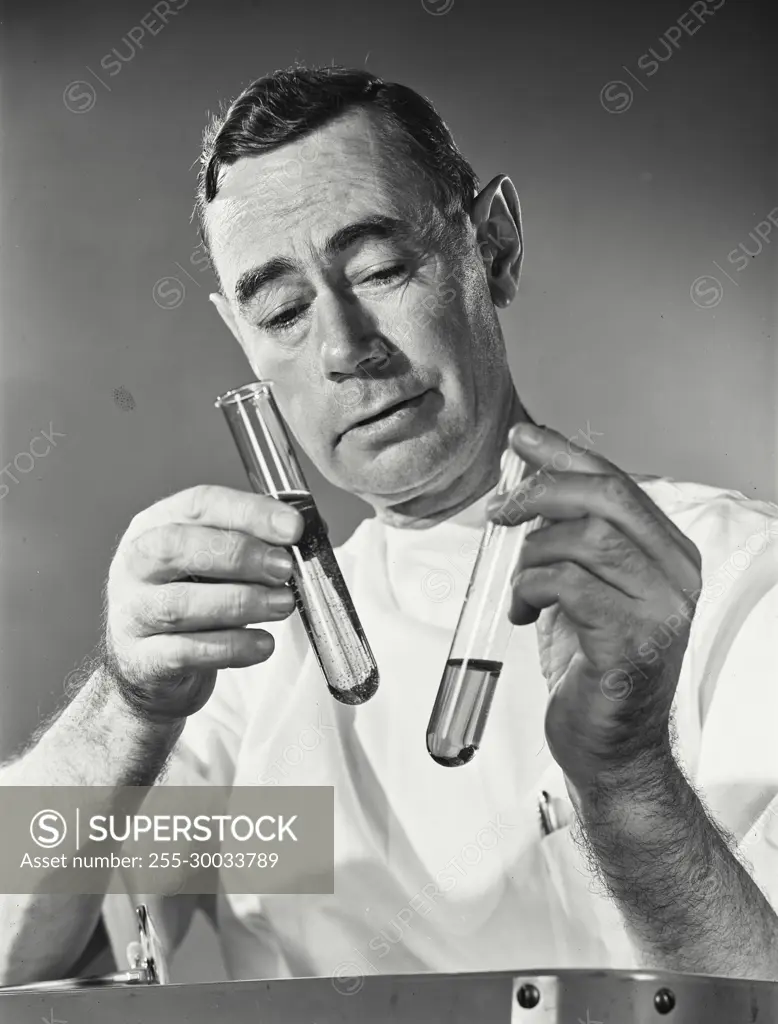 Vintage Photograph. Man in white coat looks at test tubes in studio portrait.