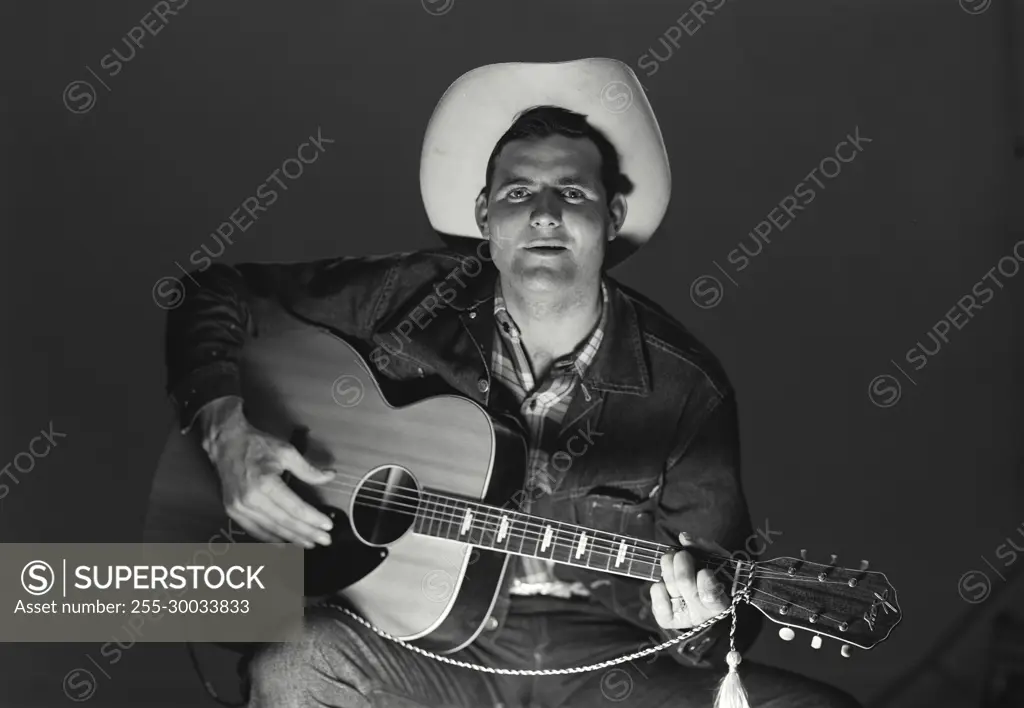 Vintage Photograph. Man sits playing guitar sings wearing cowboy hat.