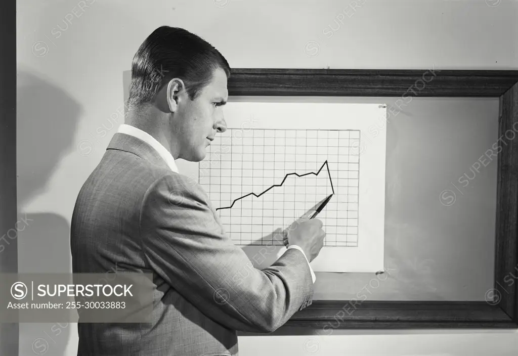 Vintage Photograph. Man points to chart showing declining numers as he looks unhappily to right of frame.