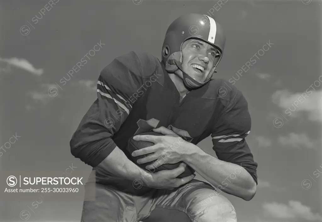 Vintage Photograph. Man runs holding football with clouds behind him.