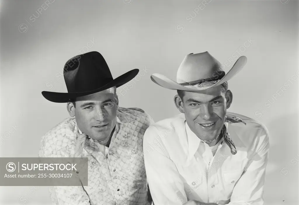 Vintage Photograph. Two men sit next to each other in studio portrait wearing cowboy hats one wears a bandana around neck.