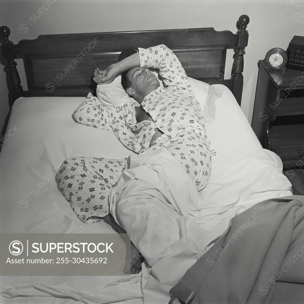 Vintage Photograph. Man lays in bed with fever he is not covered by the blankets.