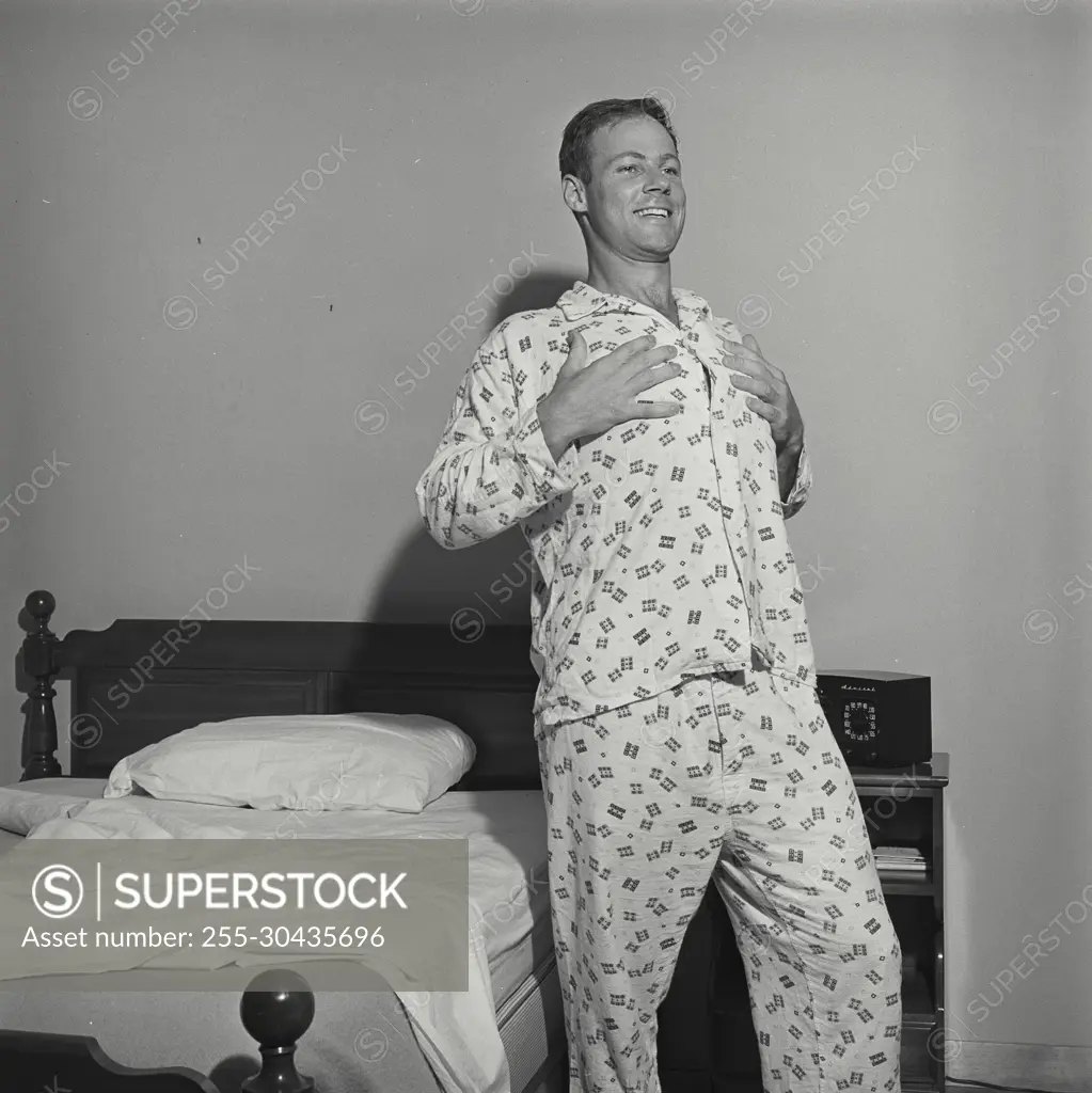 Vintage Photograph. Man stands next to bed touching breast he smiles.