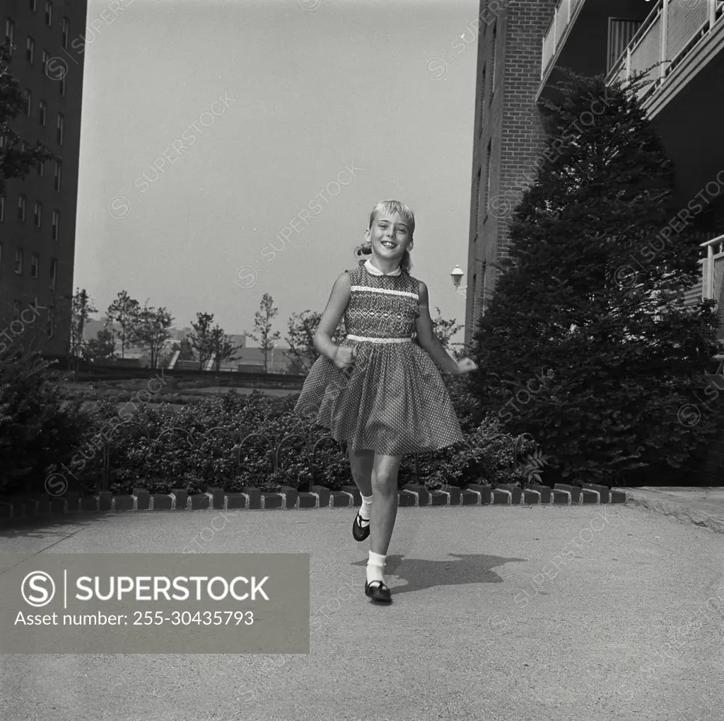 Vintage Photograph. Young girl smiles as she runs in apartment courtyard.