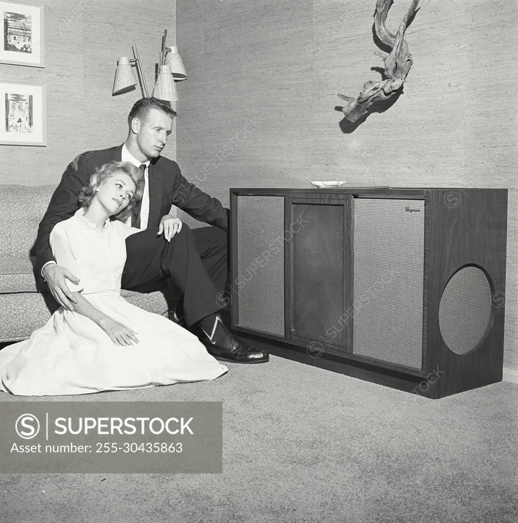 Vintage Photograph. Couple sits on couch looking over at music system.