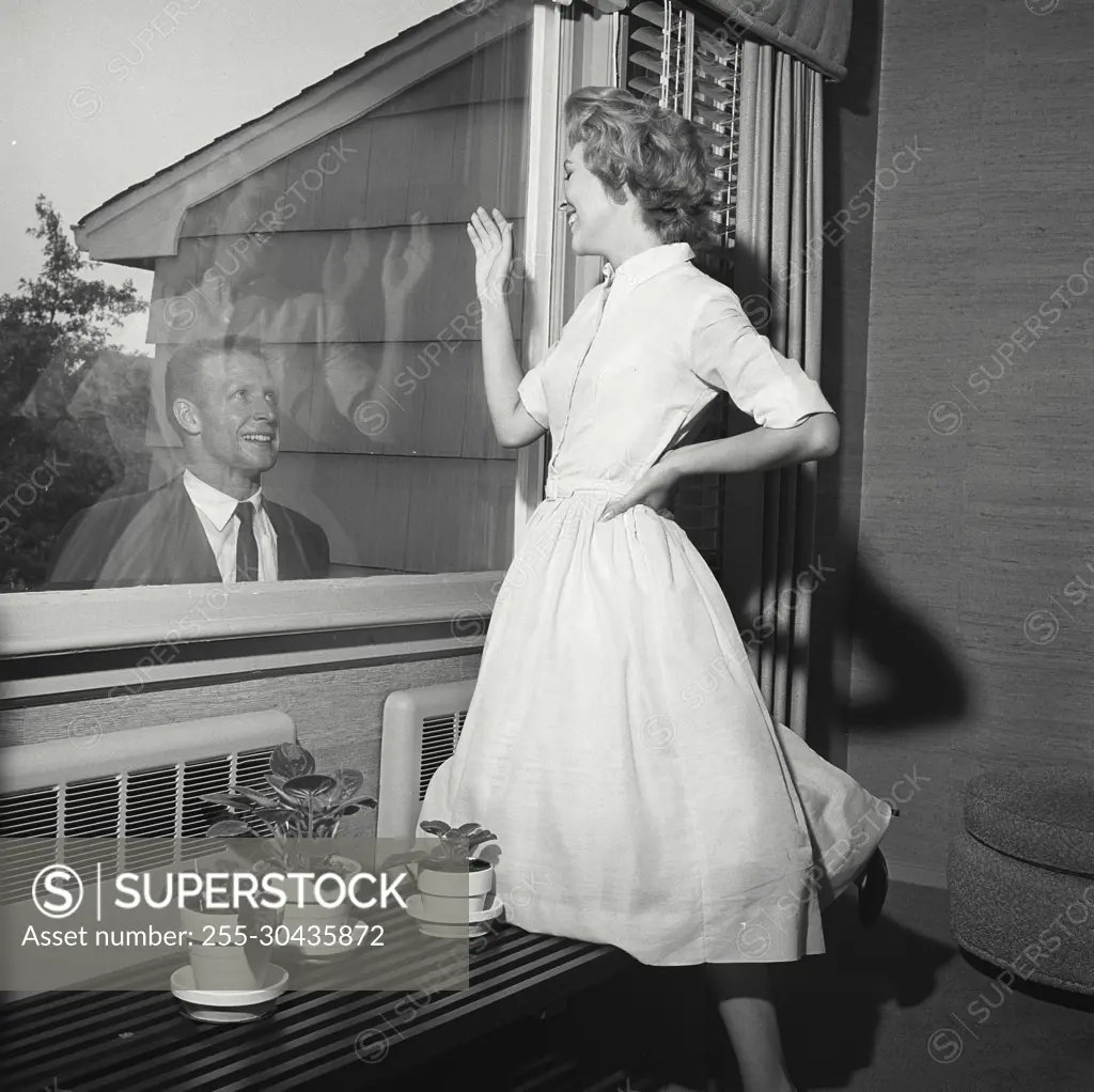 Vintage Photograph. Man stands at window while woman waves to him.