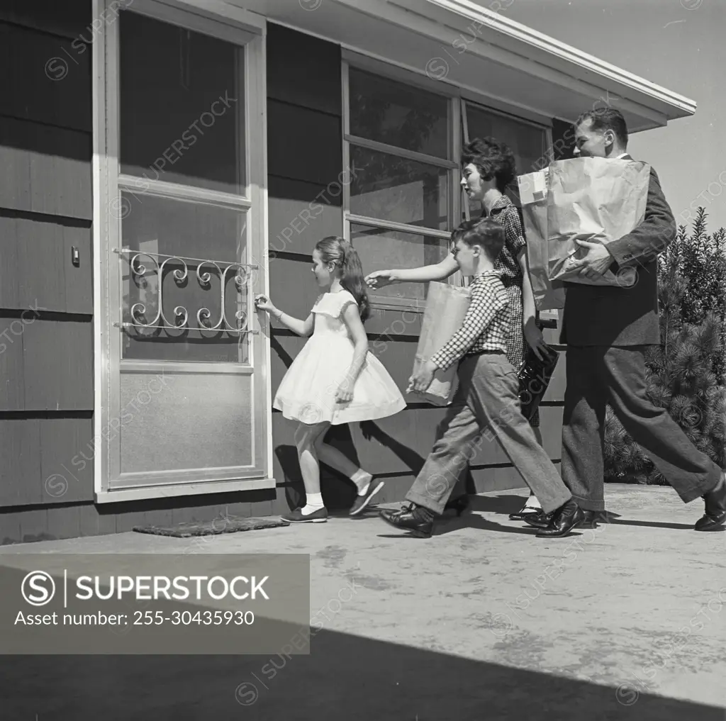 Vintage Photograph. Family carries groceries to door while little girl reaches to open it.