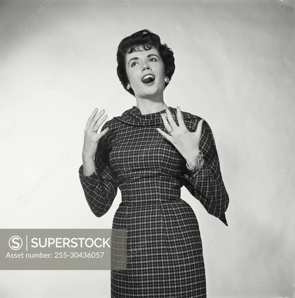 Vintage Photograph. Woman stands with her hands up singing she wears a checkered dress for studio portrait.