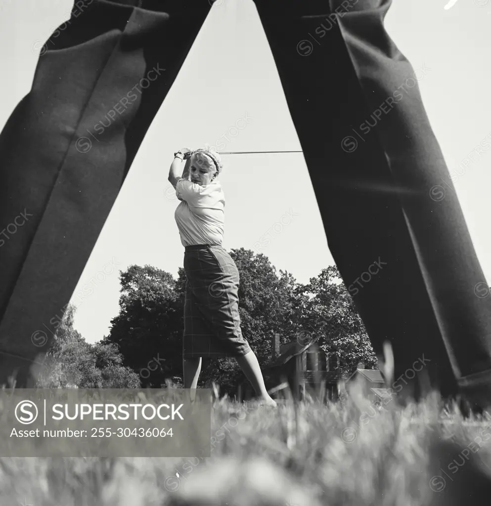 Vintage Photograph. Woman at top of swing of golf club between the legs of someone.