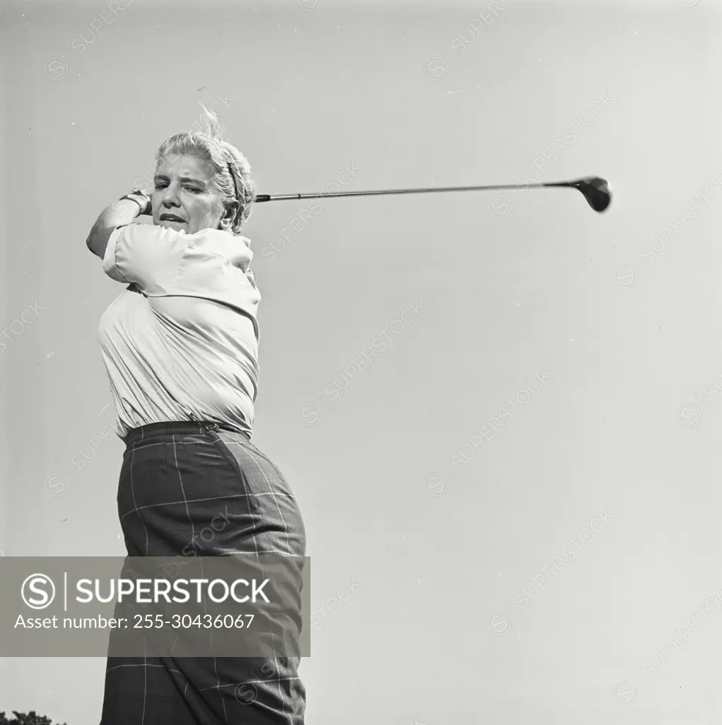 Vintage Photograph. Woman swings her golf club back as she looks to the ground.