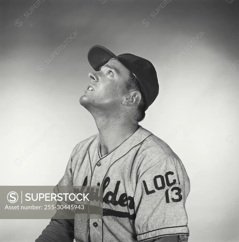 Vintage Photograph. Man sits for studio portrait looking up to the top left of frame wearing baseball uniform.