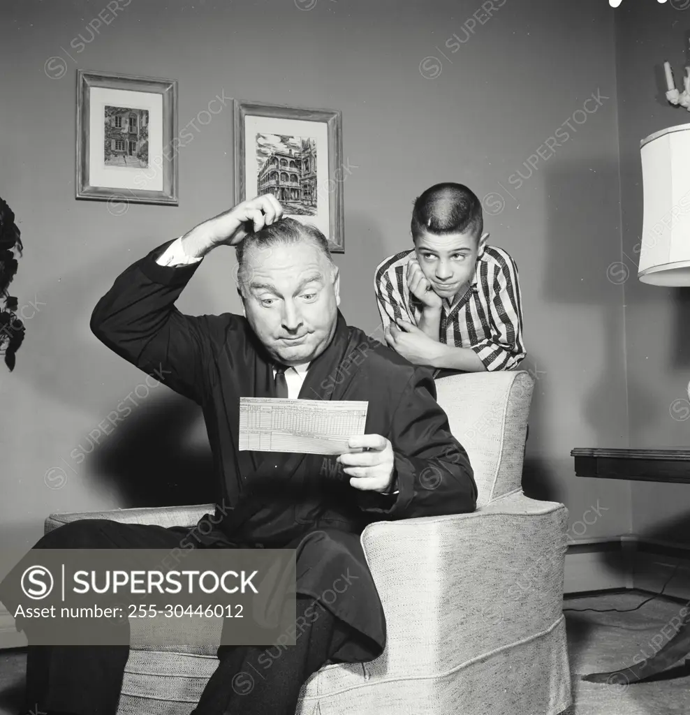 Vintage Photograph. Father scratches his head as he looks at childs report card who stands behind him.