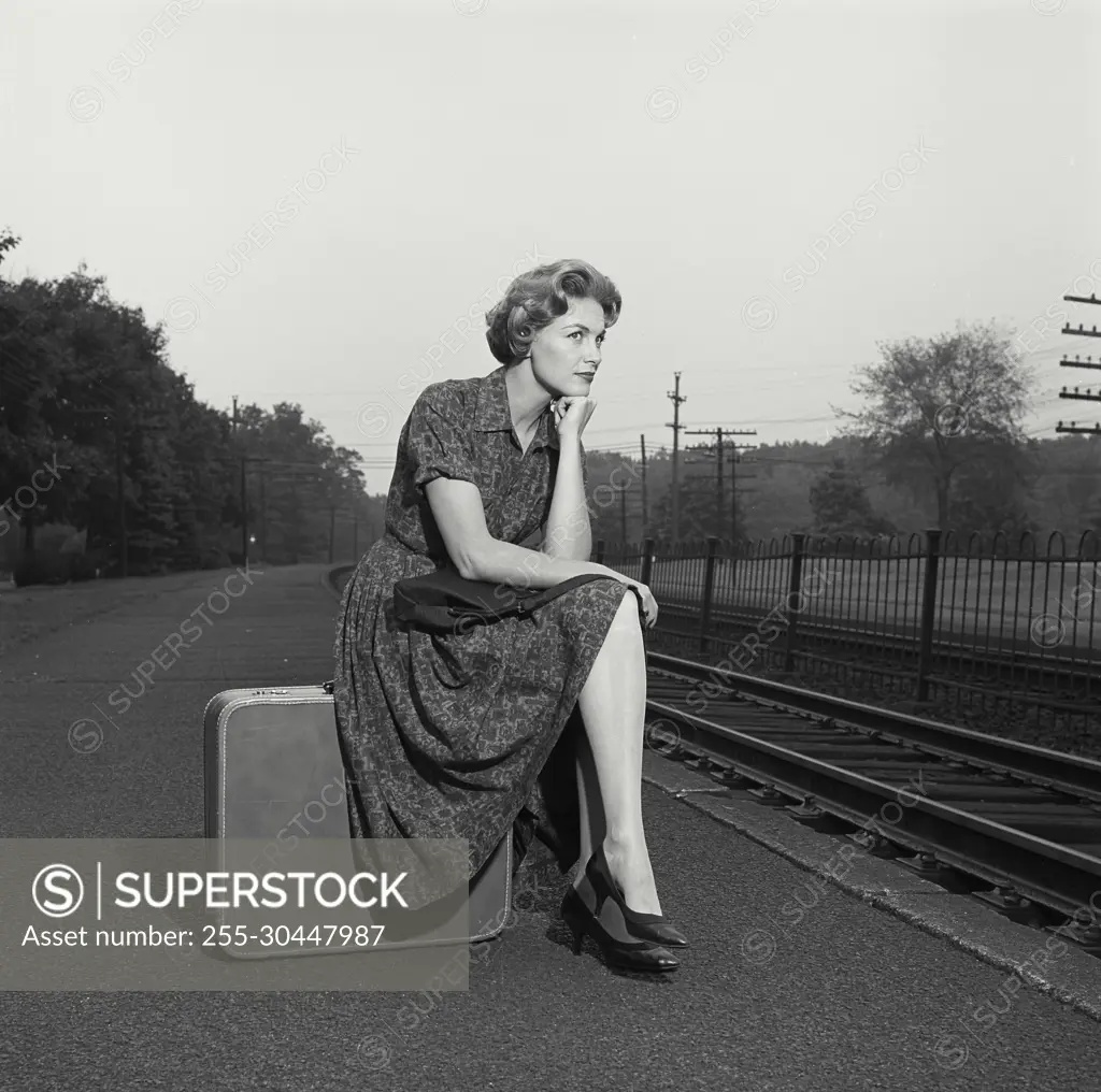 Vintage Photograph. Woman in dress sitting on suitcase.