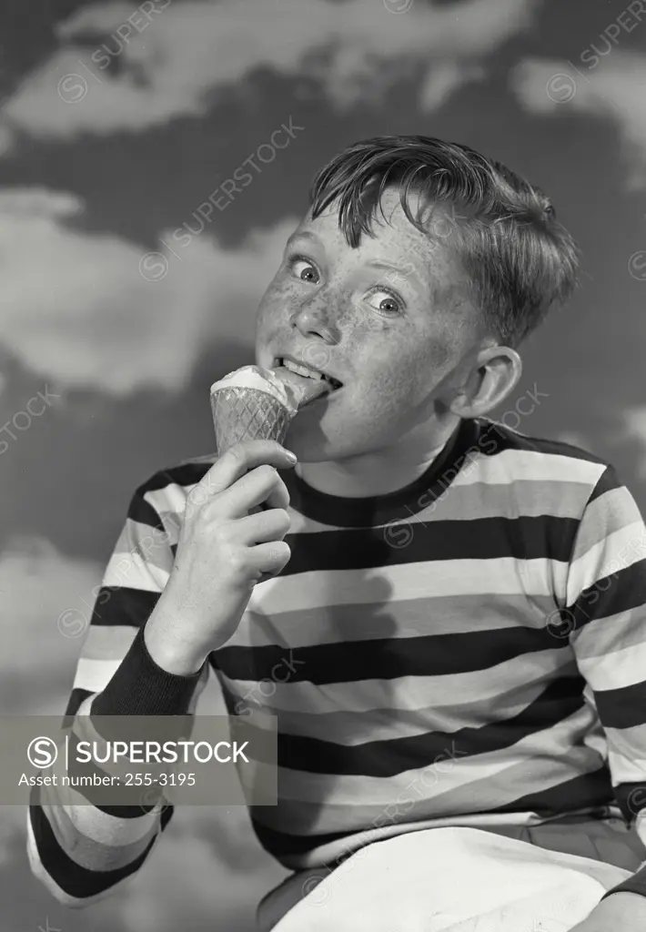 Vintage photograph. Young boy in striped shirt licking ice cream cone looking at camera