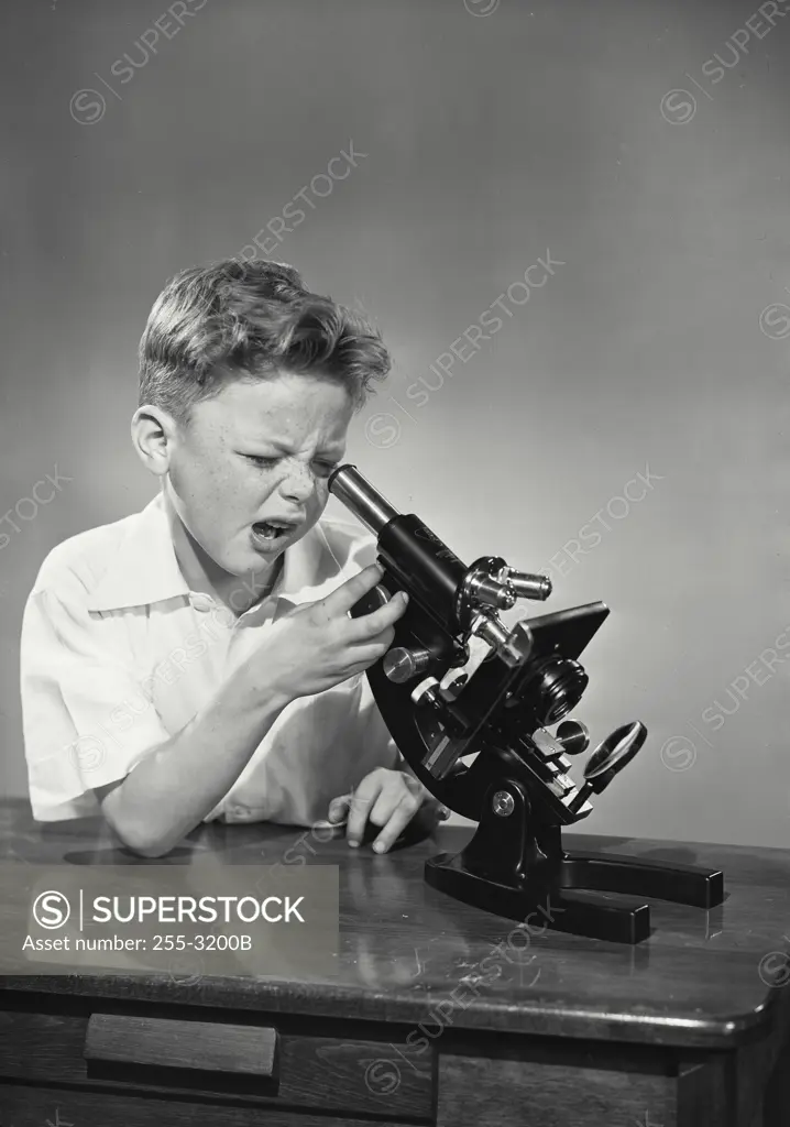 Vintage Photograph. young boy making funny expression looking into microscope on table