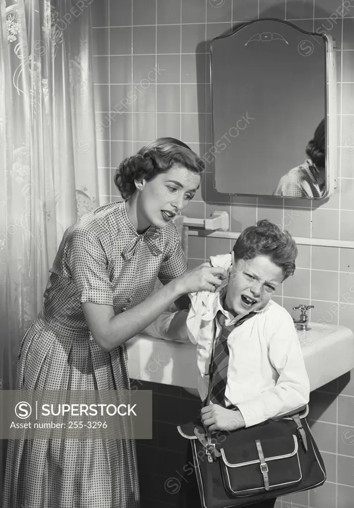 Vintage photograph. Mother cleaning unhappy young boys ear.