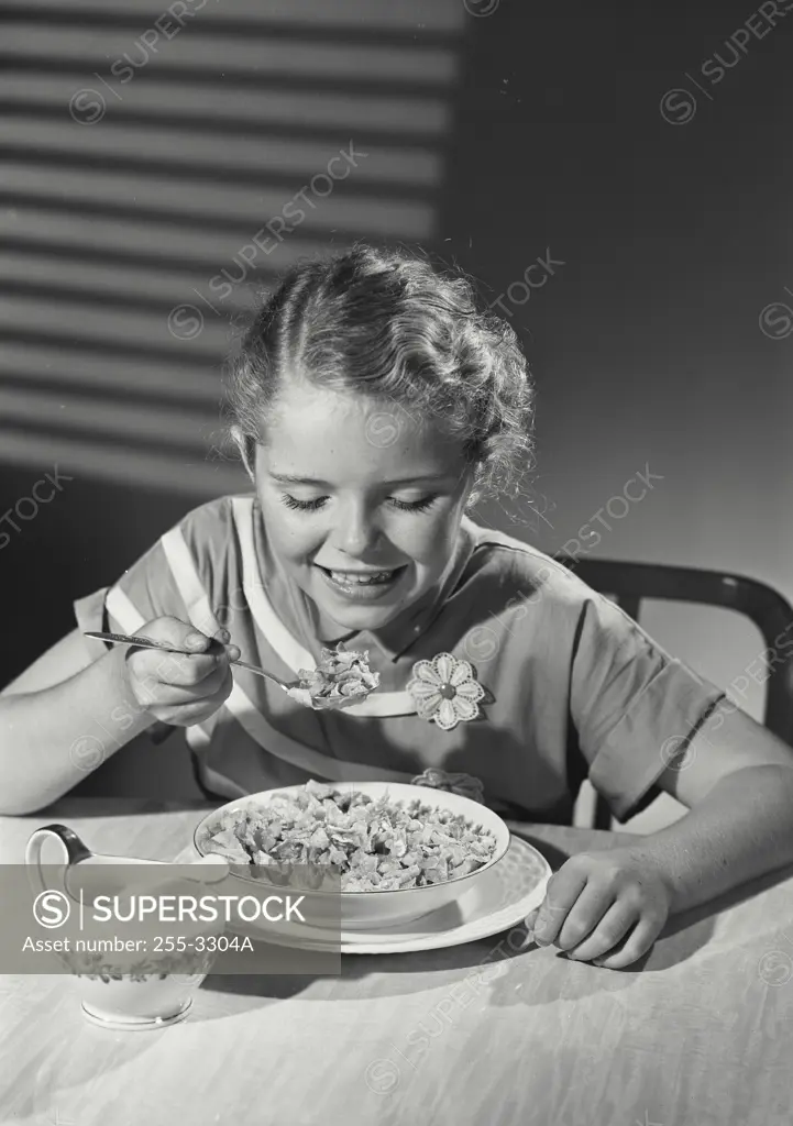 Vintage Photograph. Young girl in floral dress eating bowl of cereal