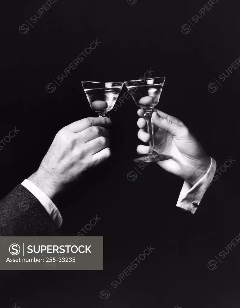 Two hands toasting with martini against black background