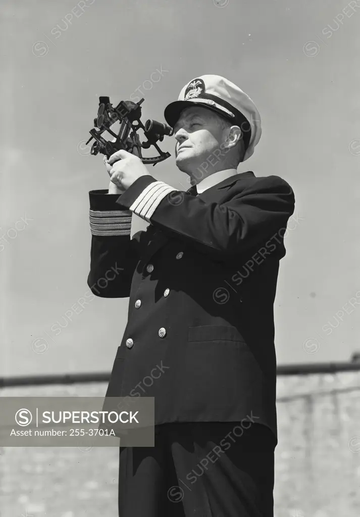 Vintage Photograph. Man in captains uniform standing and looking through sailor protractor off into the distance