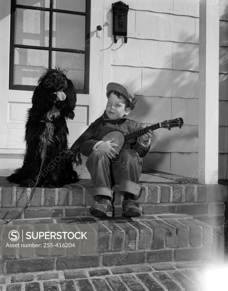 Boy playing on banjo and sitting at steps with dog