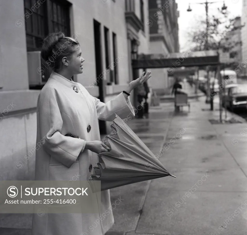 Young woman with folded umbrella checking if raining