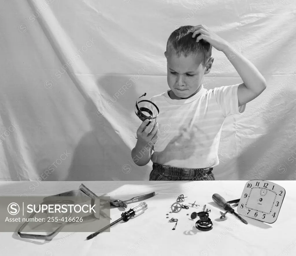 Boy in thoughts holding clock's parts