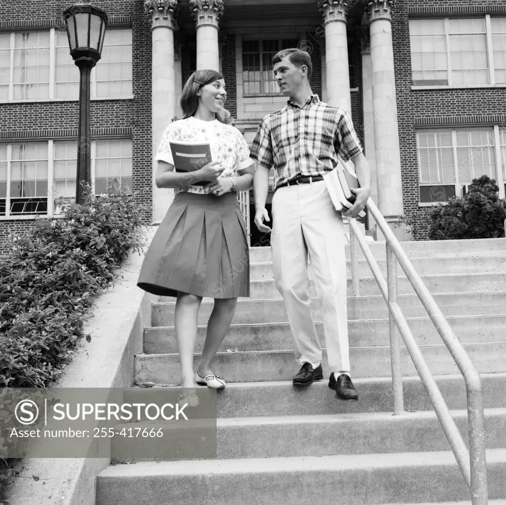 Young couple carrying books on steps outside university