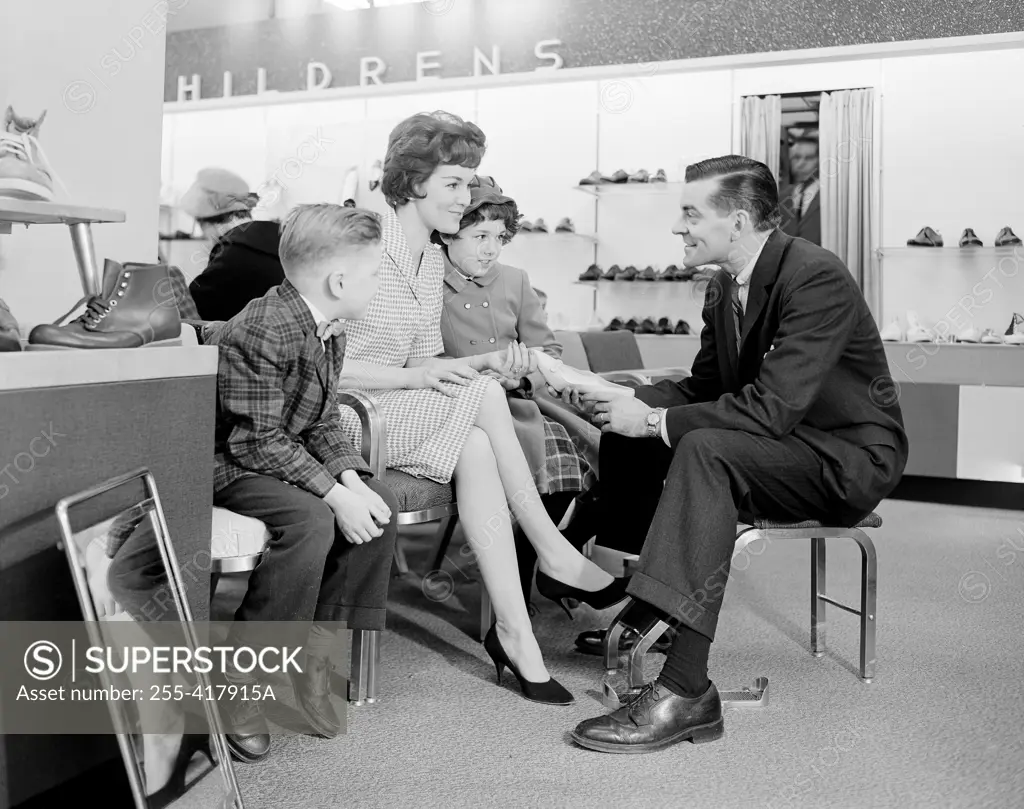 Shop assistant showing women's shoe to mother with son and daughter