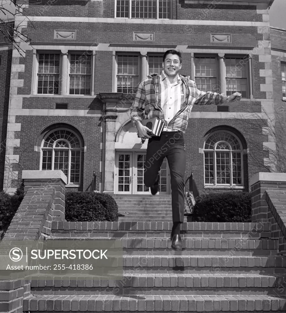 Male student jumping down steps outside university